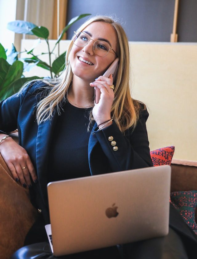 Woman in blue long sleeve shirt sitting on a brown couch taking a call