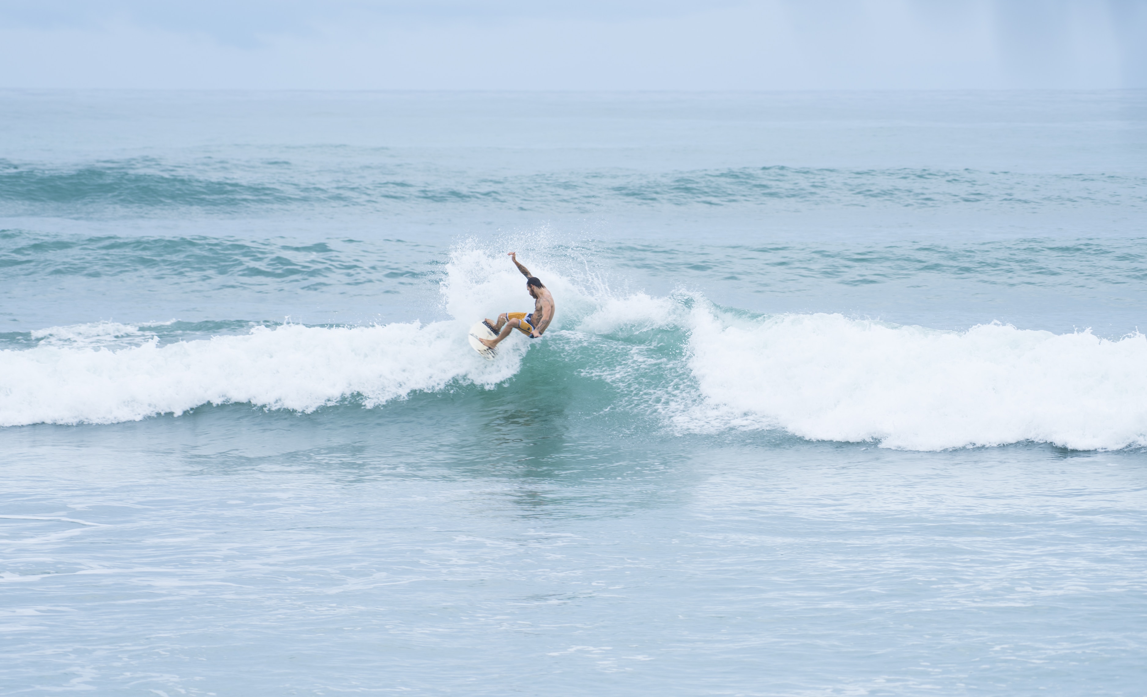 Man riding a surfboard facing the waves on the ocean and beach.